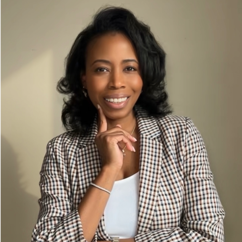 Starr Howard smiling with her hand at her chin, wearing a houndstooth blazer